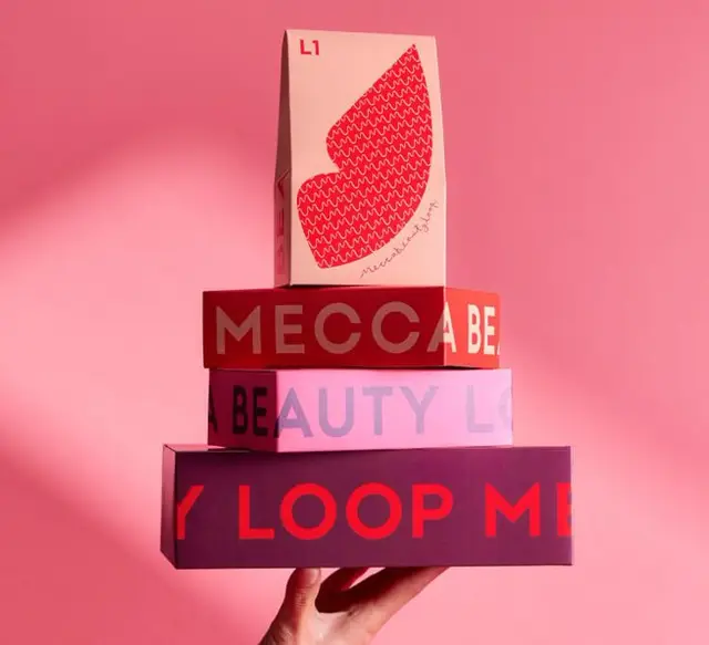 Stacked pink and red Mecca beauty packaging held by hand