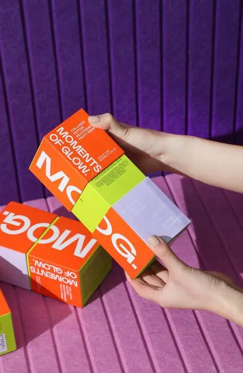 Bright orange "MOMENTS OF GLOW" skincare boxes on purple ribbed backdrop