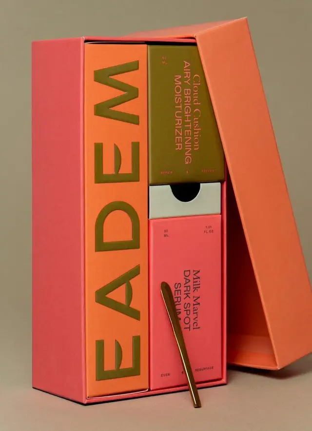 Coral presentation box with olive moisturizer and pink dark-spot serum, gold spatula