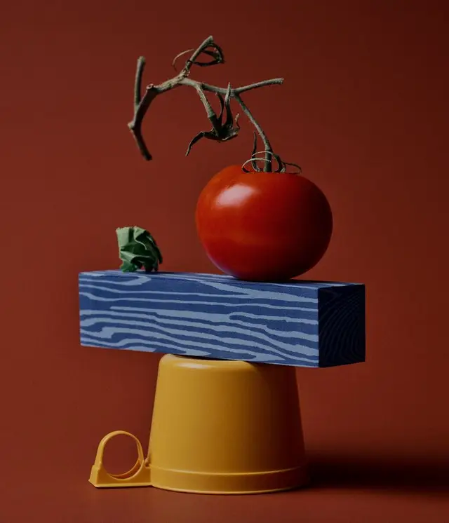 Ripe tomato on blue painted wood over yellow plastic cup — minimalist still life