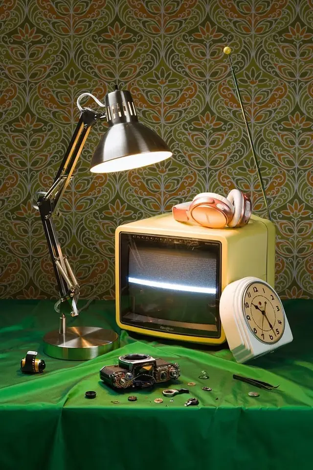 Still life: yellow mini CRT TV, chrome desk lamp, disassembled camera on green cloth