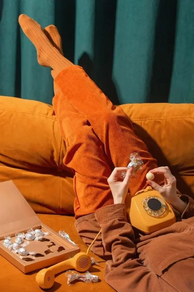 Retro rotary phone on orange sofa with corduroy pants and foil-wrapped chocolates