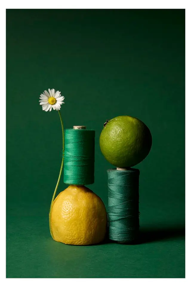 Emerald thread spools balanced on lemon and lime — studio still life