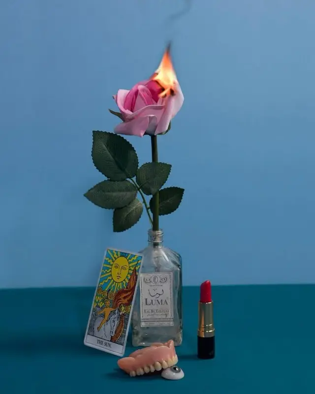Burning pink rose still life with tarot, lipstick, dentures, and glass eye