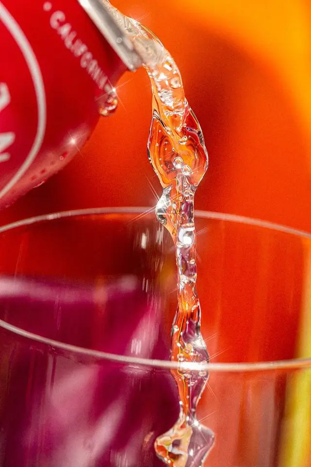 Macro shot of clear liquid poured from red can into glass with orange backdrop