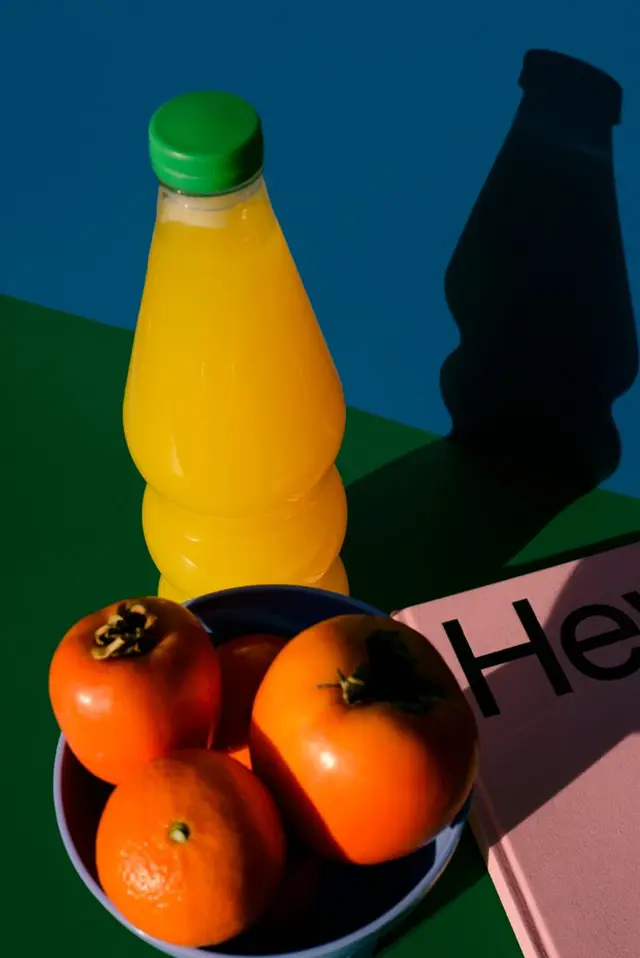 Still life — orange juice bottle, persimmons and pink book