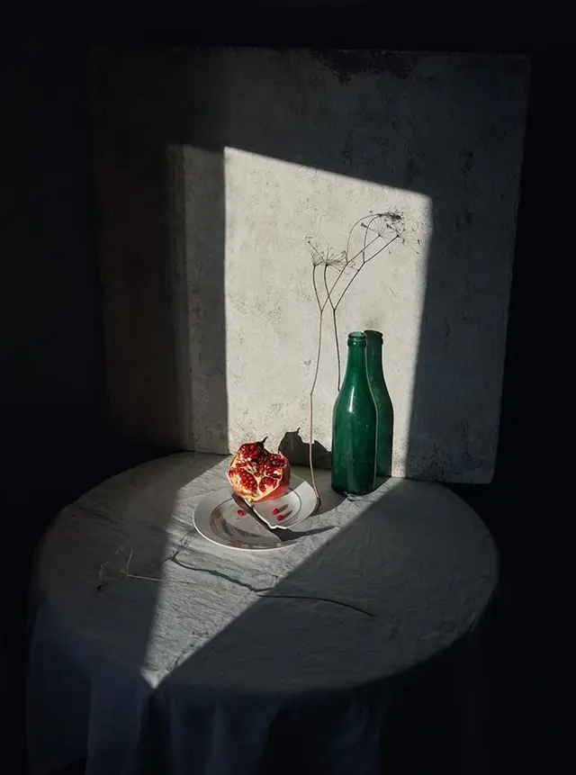 Pomegranate still life with green bottle and dried seedheads