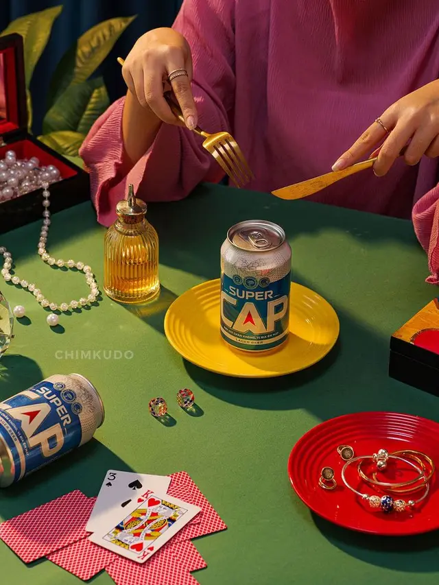 SUPER CAP can on yellow plate — still life with gold cutlery, pearls and playing cards