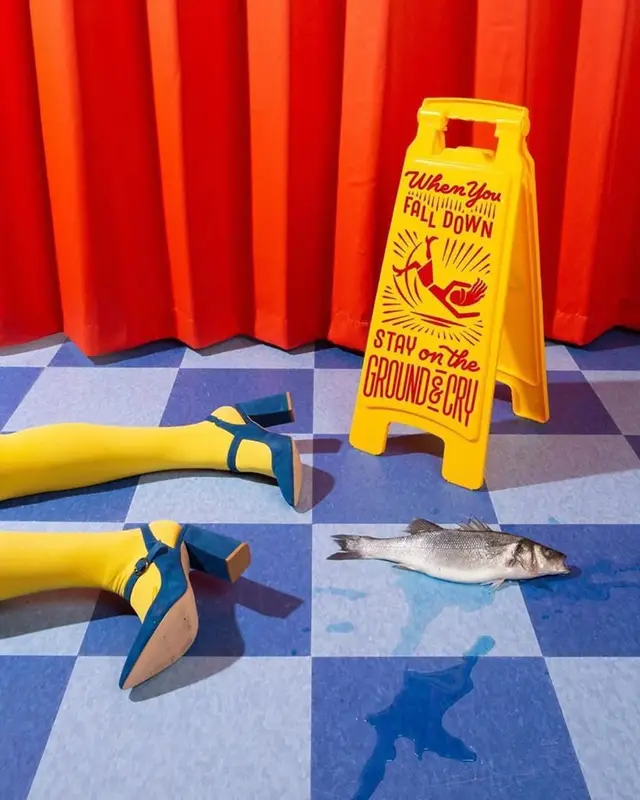 Staged still-life: yellow caution sign, fallen legs and fish on blue checkerboard