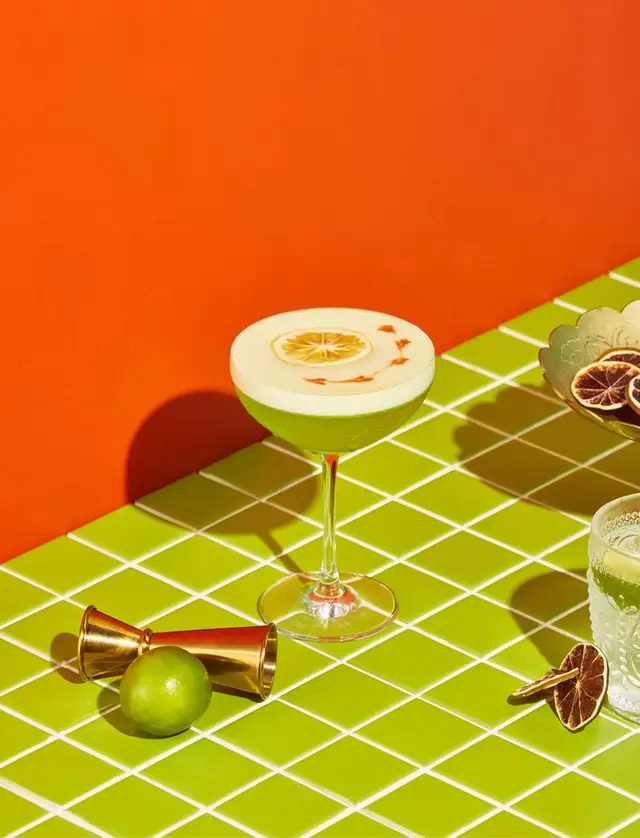 Lime-green coupe cocktail on chartreuse tiled tabletop with orange backdrop