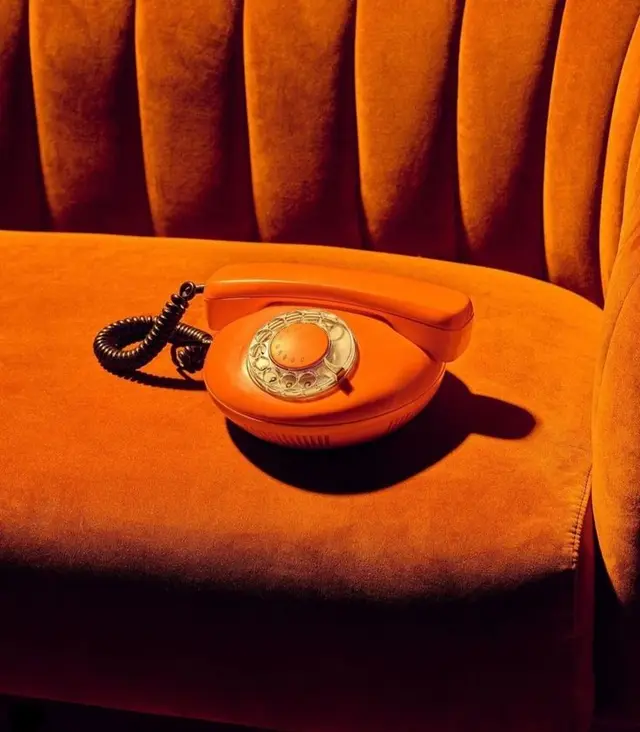 Orange rotary telephone on velvet tufted sofa