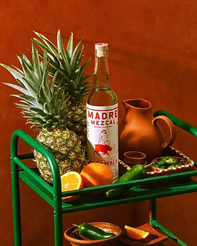 Madre Mezcal bottle with pineapples, oranges and terracotta pitcher on green bar cart