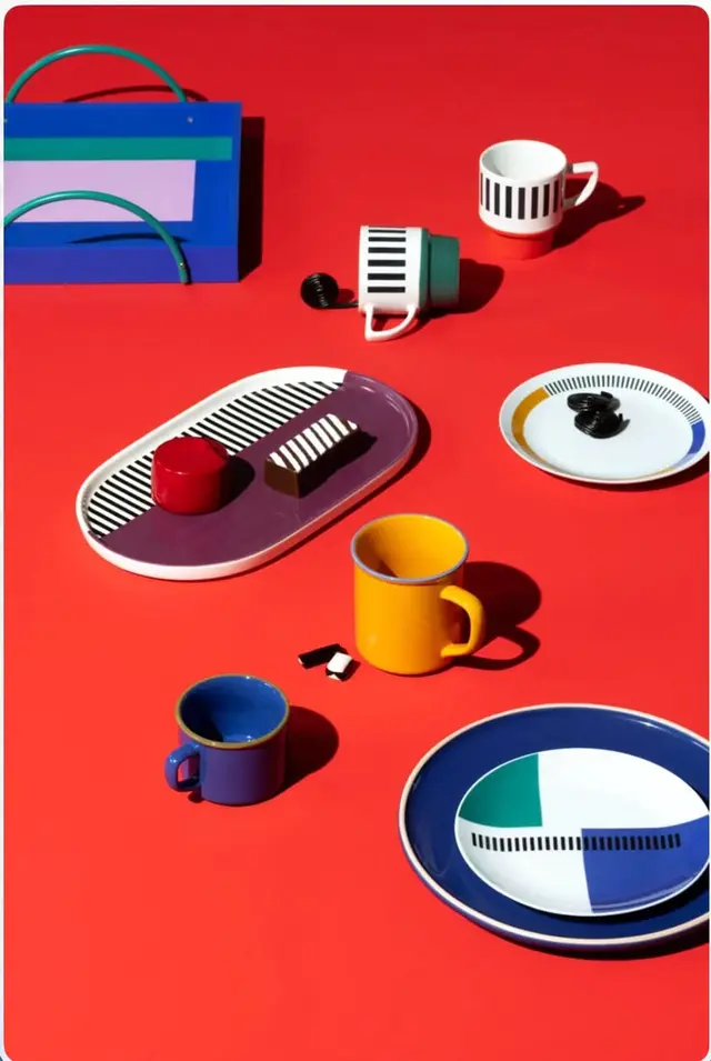 Color-blocked ceramic plates and enamel mugs on red tabletop