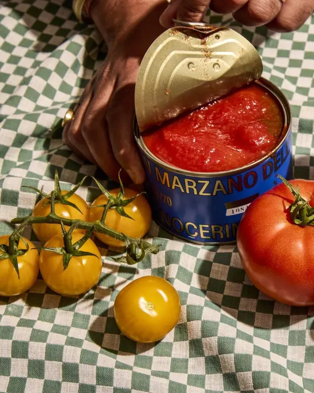 Opened Marzano tin of peeled tomatoes with yellow cherry tomatoes on green checkered cloth