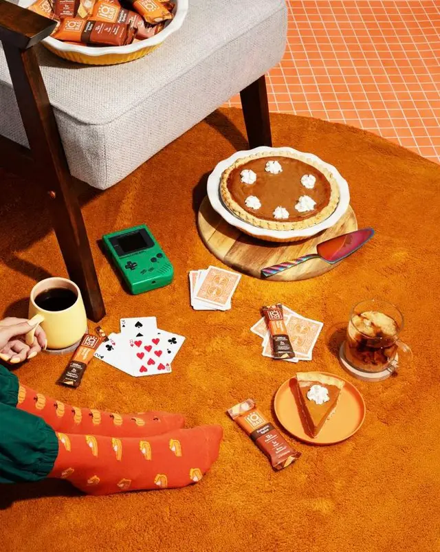 Cozy autumn snack spread with pumpkin pie, green handheld console, and playing cards