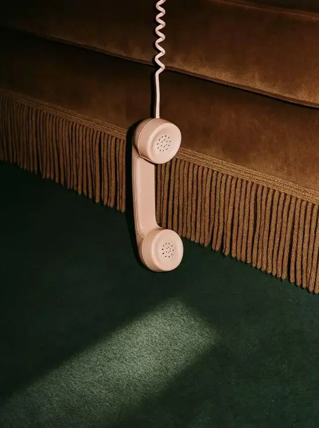 Beige retro telephone handset hanging from brown velvet sofa fringe