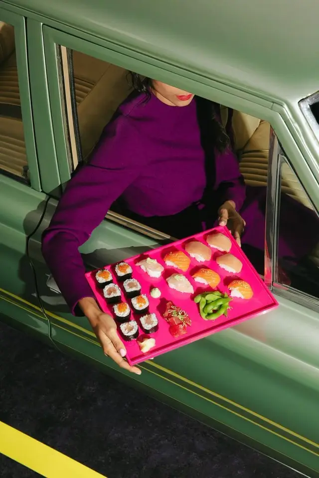 Hot-pink sushi tray handed out of green vintage sedan
