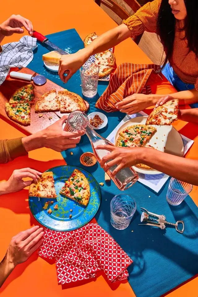 Bright flat‑lay of friends sharing pizza on orange tabletop