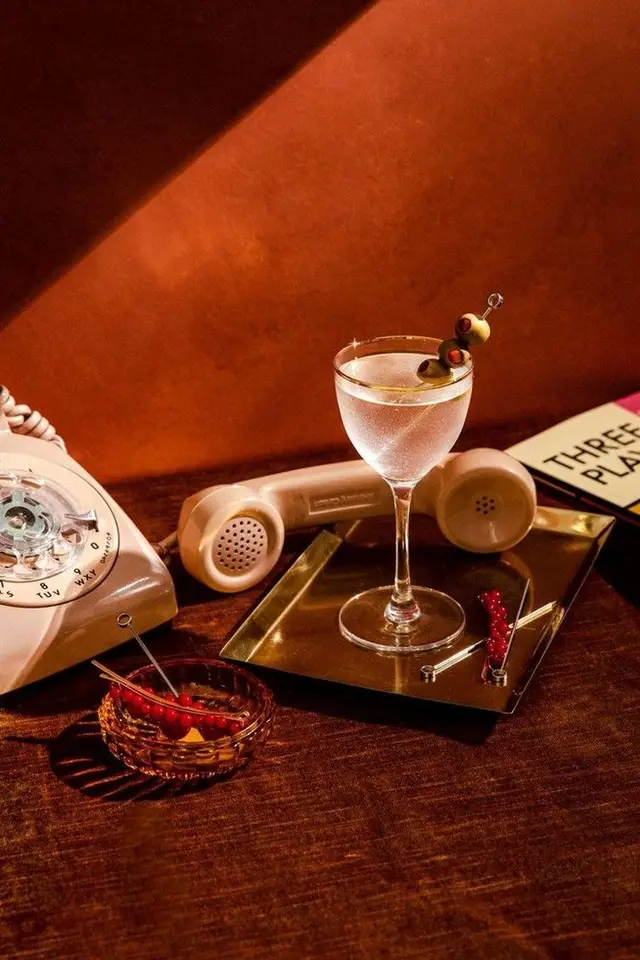 Retro coupe cocktail with olive skewer, rotary phone and brass tray