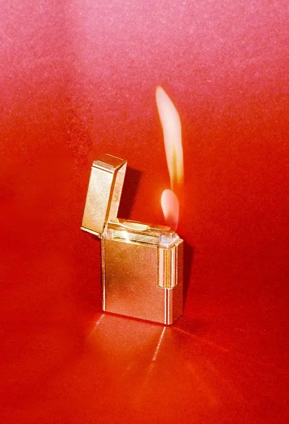 Gold textured flip-top lighter with tall flame on red backdrop