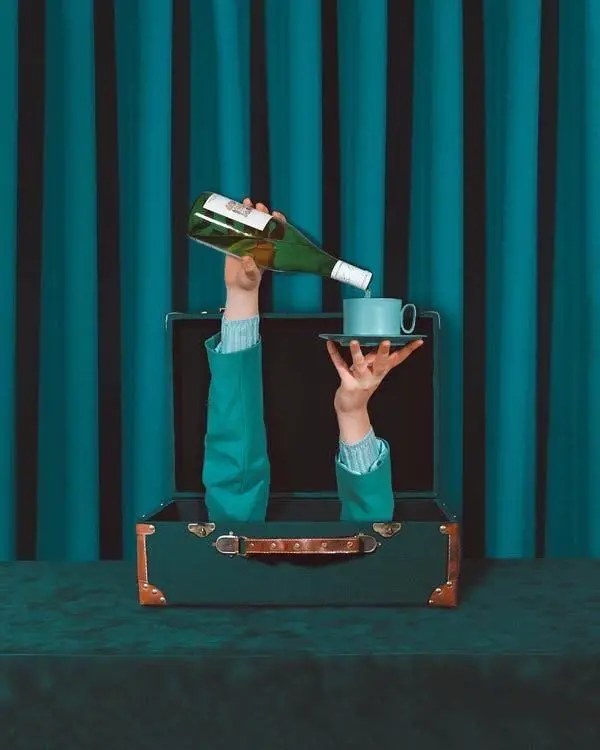 Hands Pouring Wine into Teal Cup from Vintage Suitcase — Surreal Staged Photo