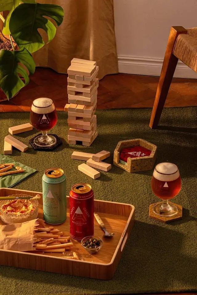 Indoor floor picnic with canned beer, snifter glasses, Jenga tower and snacks on green rug