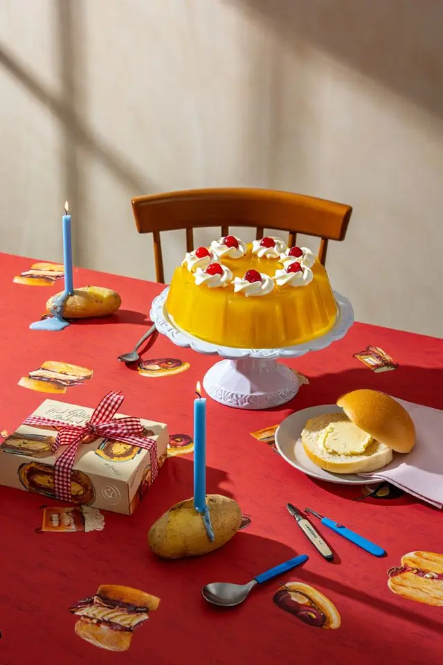 Yellow gelatin bundt with cherries on white cake stand over red sandwich-print tablecloth