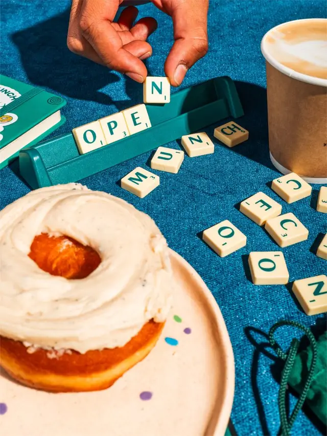 Teal tabletop flatlay: glazed donut, latte and Scrabble-style tiles spelling OPEN