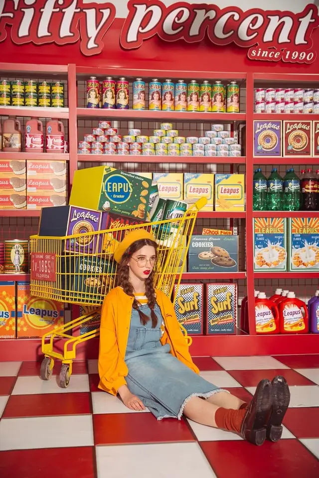 Editorial: model in mustard jacket with yellow shopping cart in retro 'Leapus' supermarket