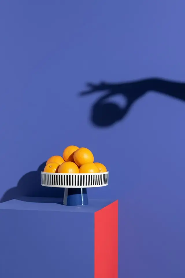 Oranges on white slatted pedestal with hand shadow on blue backdrop