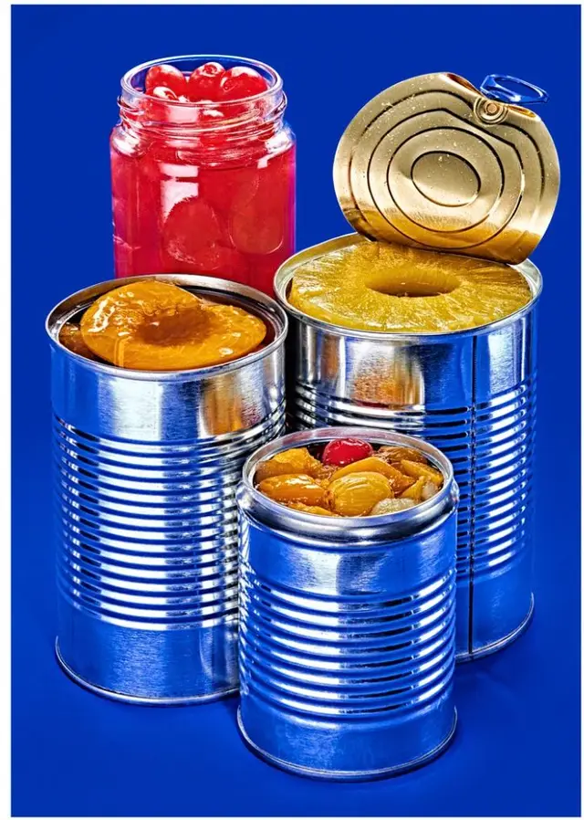 Canned fruit still life — pineapple rings, peaches and cherries in tins on blue backdrop