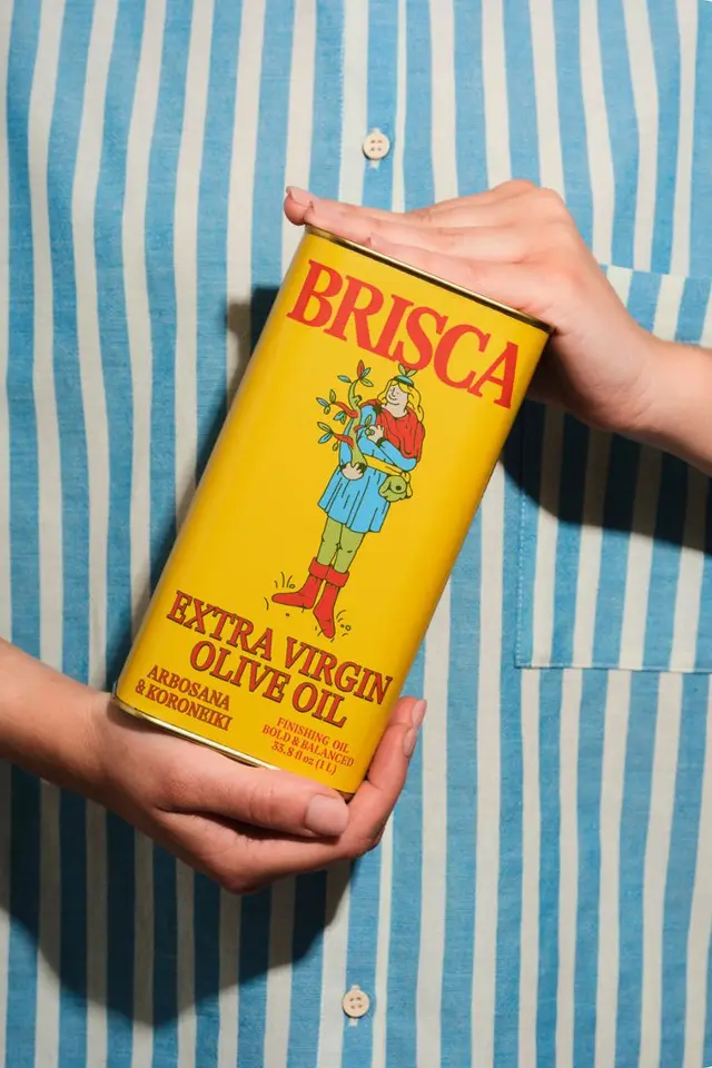 BRISCA Extra Virgin Olive Oil — yellow retro metal tin held against blue-striped shirt
