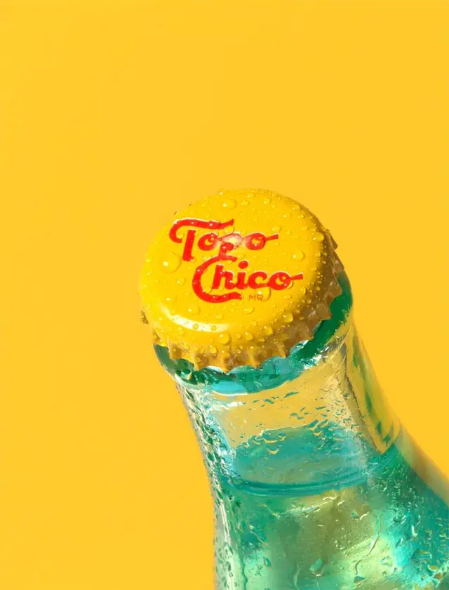 Topo Chico yellow crown cap on teal glass — close-up product photo