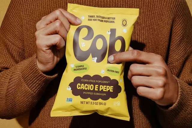 Cob Cacio e Pepe popped sorghum snack — yellow package held in brown sweater