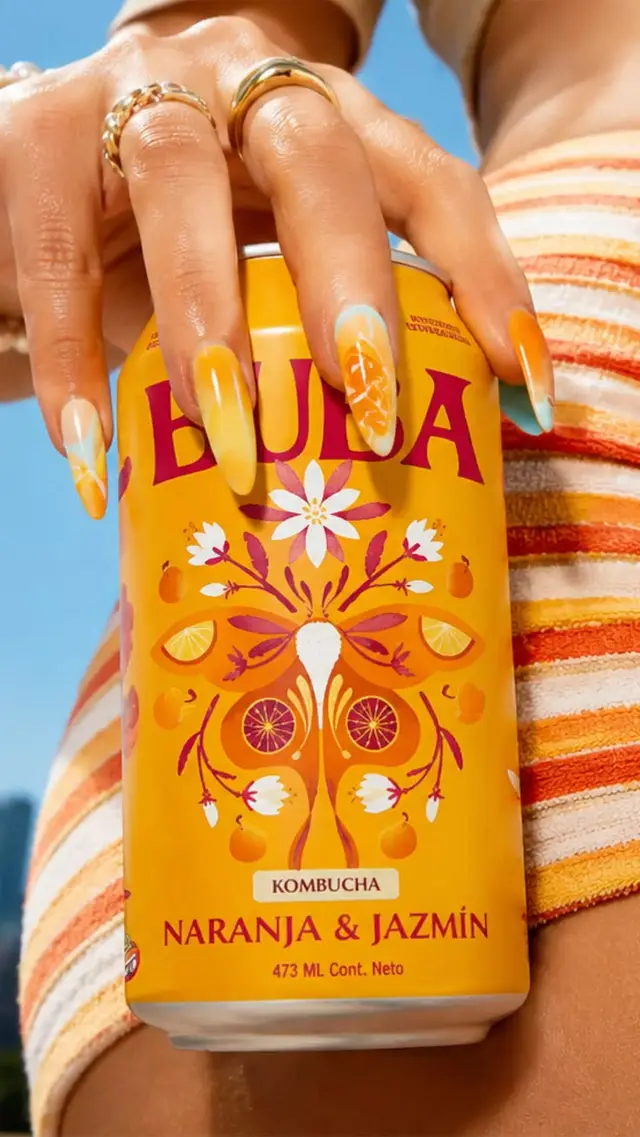 Naranja & Jazmín kombucha can held by hand with yellow-orange nail art