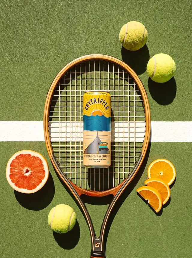 Daytripper blood-orange + pink-grapefruit can in vintage tennis racket flat lay