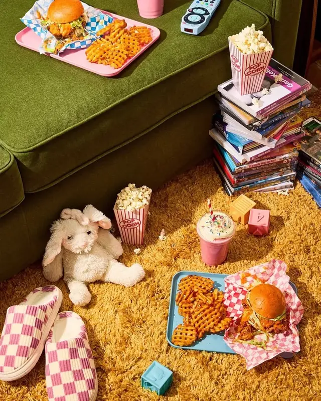 Retro movie-night snack spread on olive sofa and mustard shag carpet