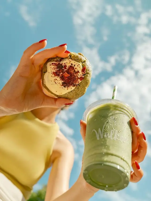 Low-angle photo: green iced latte and cream-topped green cookie against blue sky
