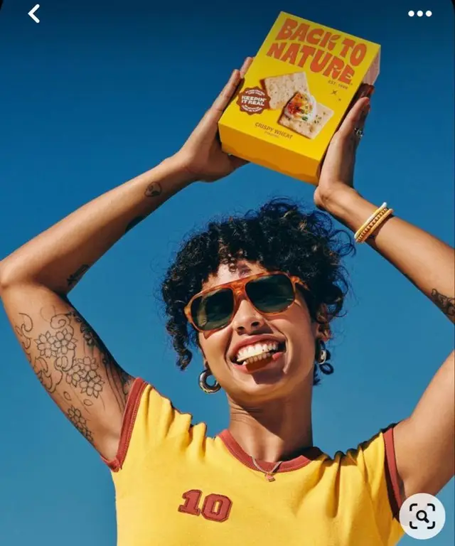 Person holding yellow 'Back to Nature' cracker box against blue sky