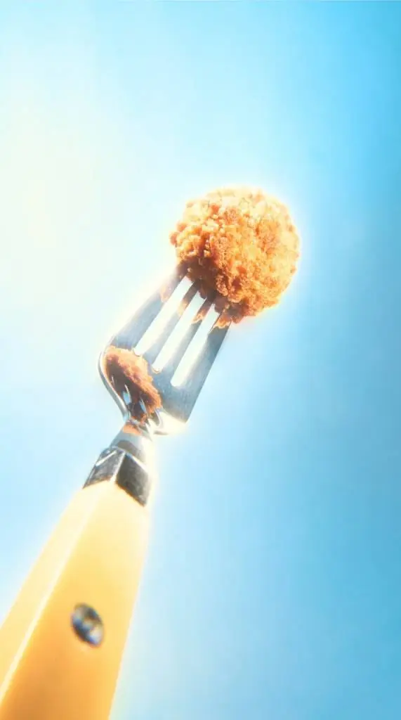 Yellow-handled fork holding a single breaded nugget against bright sky