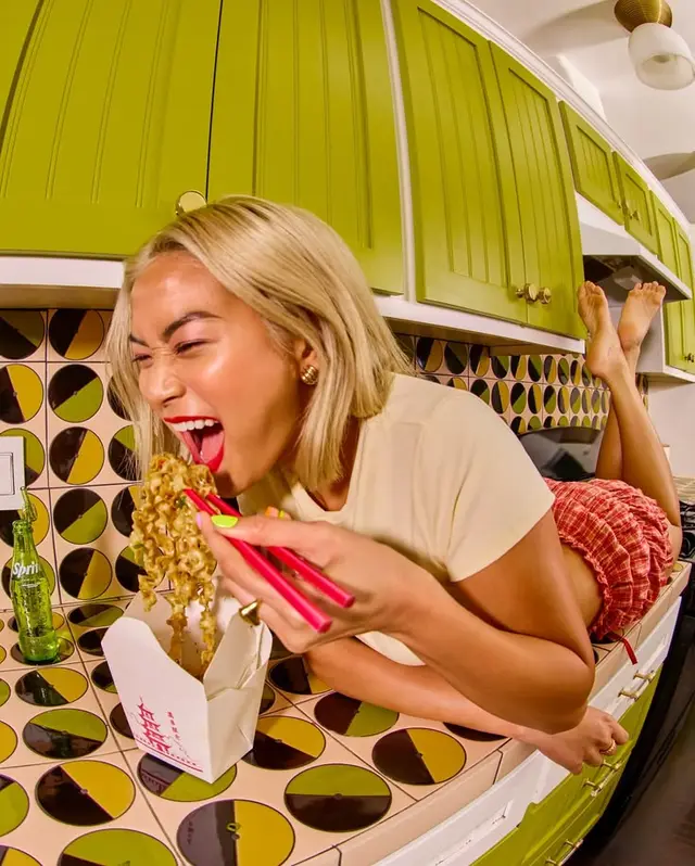Woman eating takeout noodles on countertop in lime-green retro kitchen