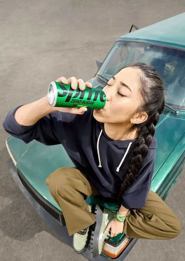 High-angle lifestyle shot: woman drinking Sprite Zero Sugar on vintage green car