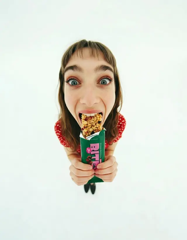 Fisheye top-down portrait: woman biting green 'BITE' granola bar