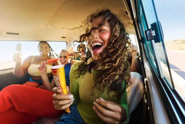 Young friends laughing in a sunlit van with ice cream on a road trip