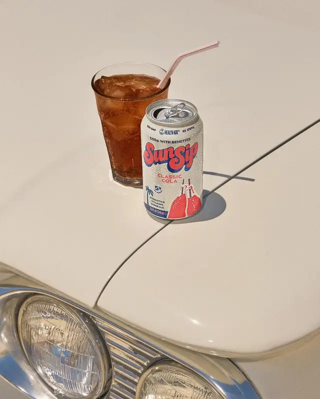 SunSip Classic Cola can and iced drink on cream vintage car hood