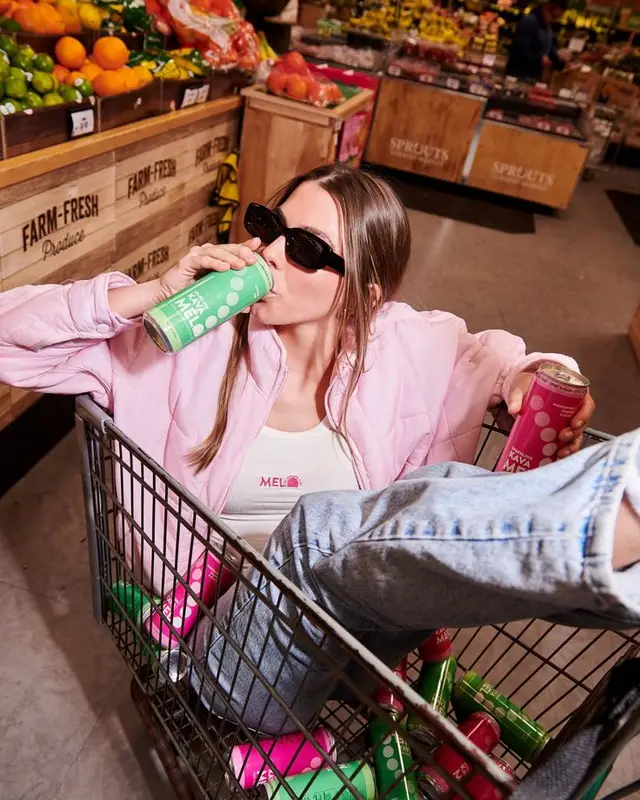 Woman lounging in shopping cart drinking canned beverage in produce aisle