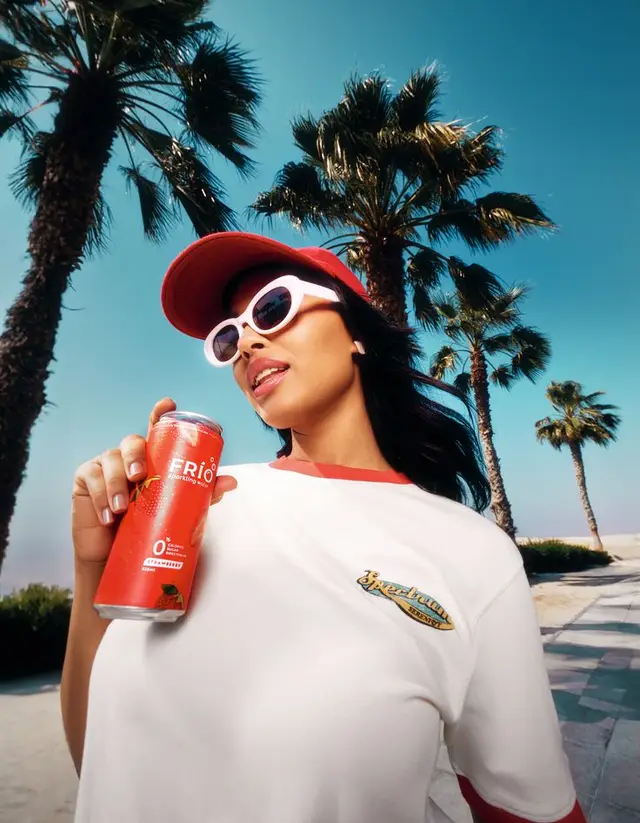 Low-angle summer portrait: woman with red FRÍO can under palm trees
