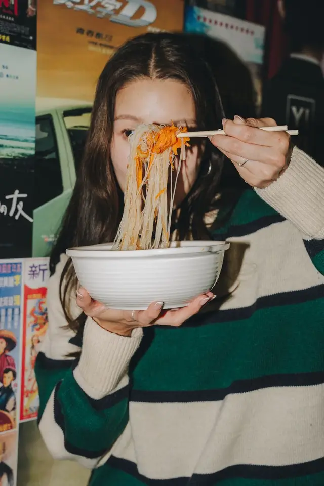 Person eating rice vermicelli from white bowl with chopsticks, retro poster backdrop