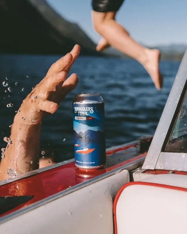 Smugglers Trail can on red boat gunwale with swimmer jumping into mountain lake