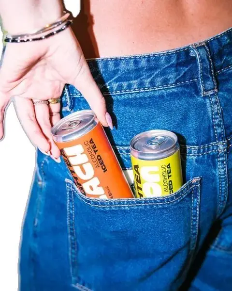 Orange and yellow slim cans of alcoholic iced tea tucked into denim back pocket